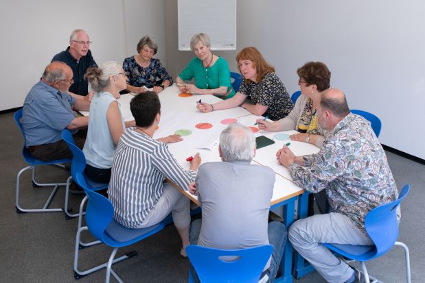 Eine Gruppe von Menschen unterschiedlichen Alters sitzt gemeinsam am Tisch zum Forschenden Lernen